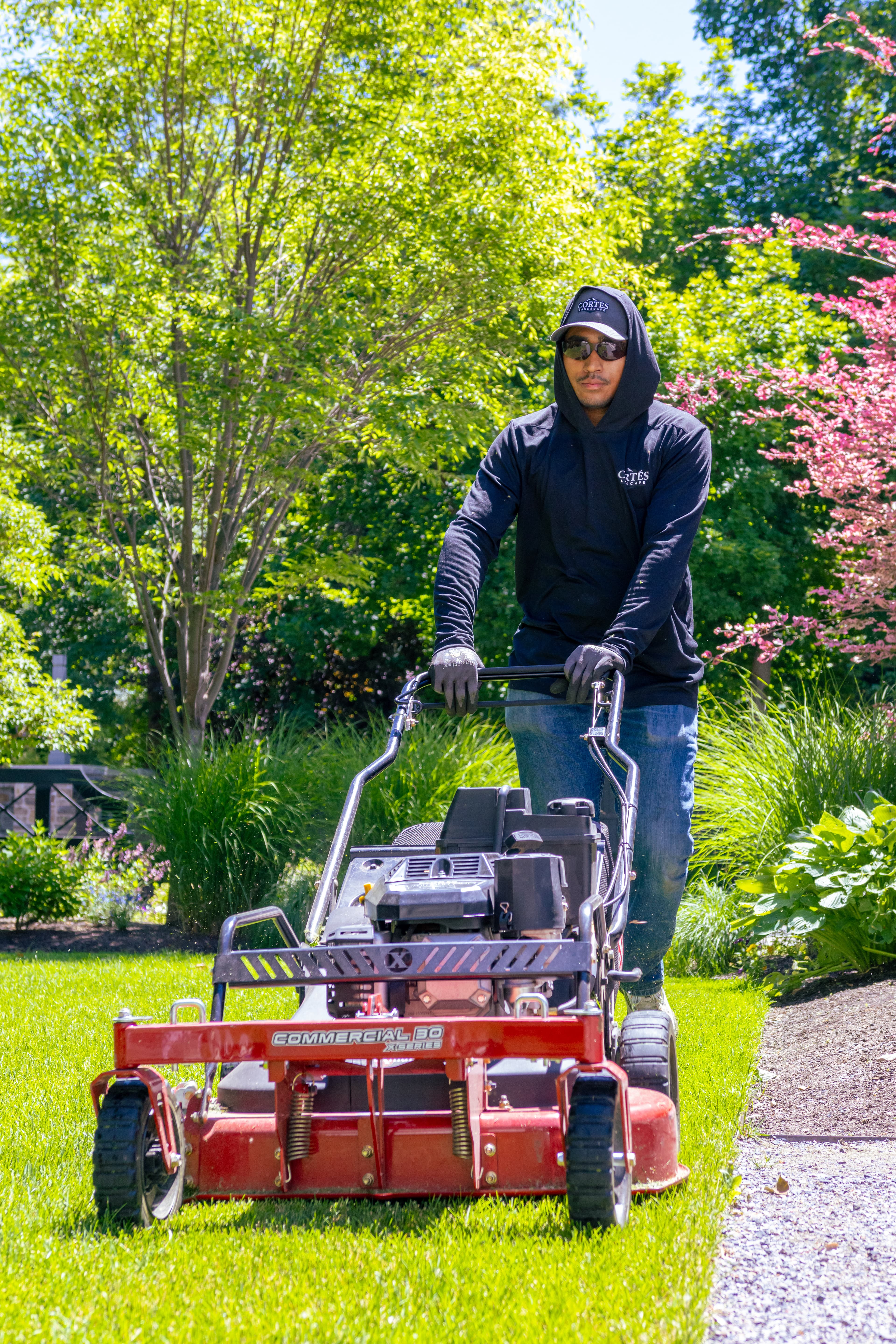 Man in a black hoodie operating a red commercial lawnmower on a lush green lawn.