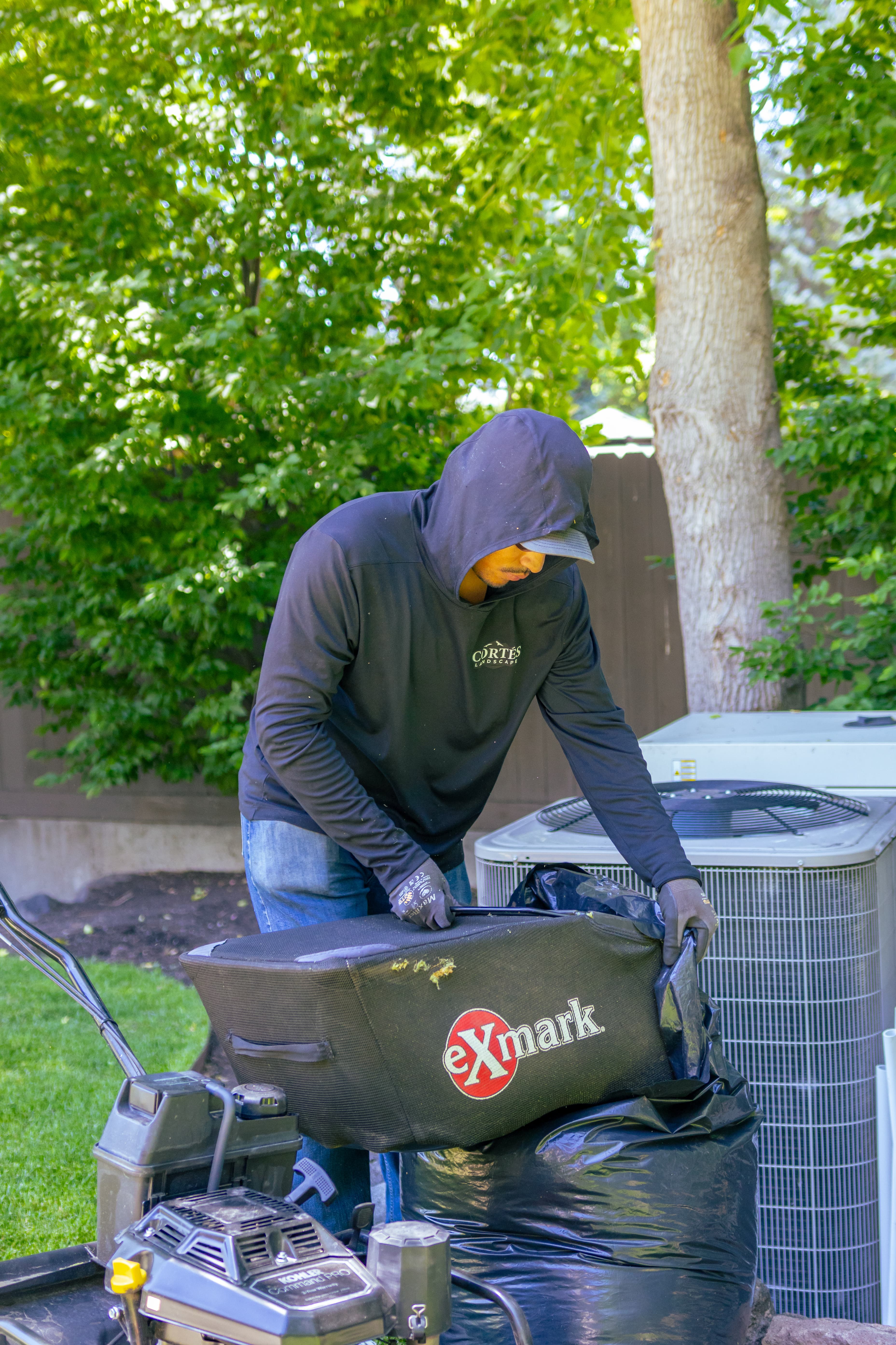 Landscaper empties an Exmark grass catcher bag into a large black trash bag.