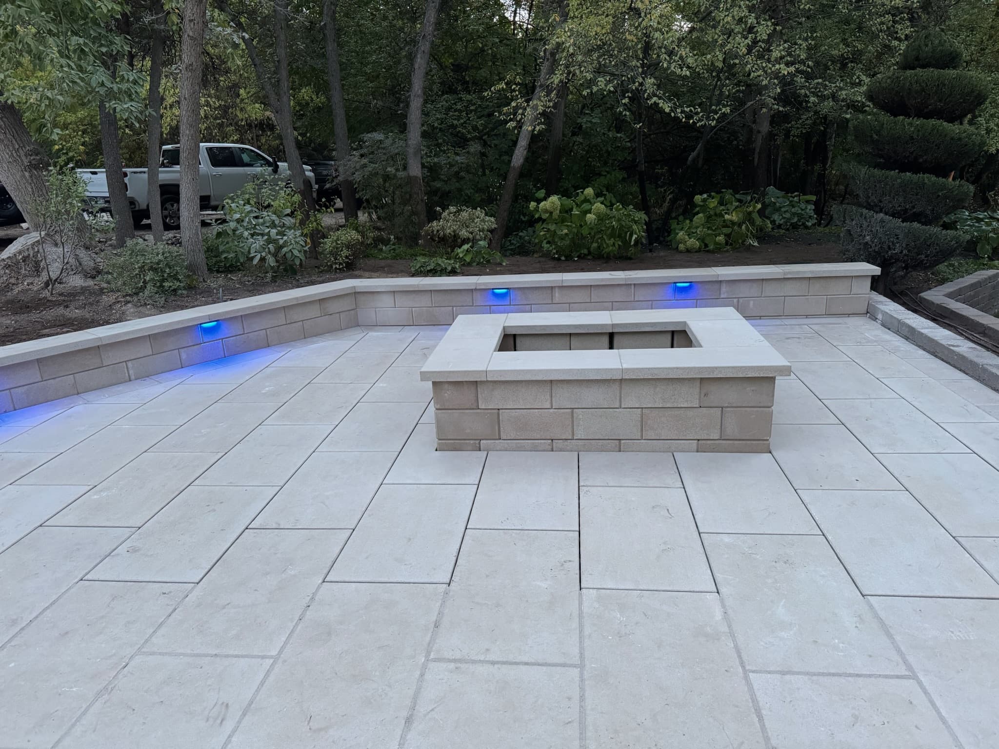 Modern stone patio featuring a square fire pit and blue LED accent lighting on walls.